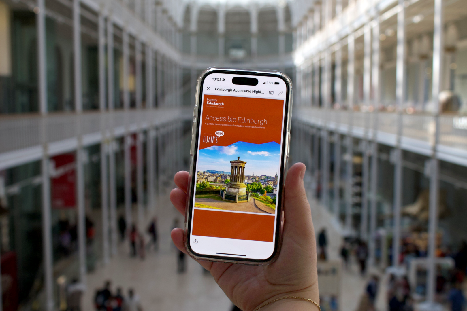 Hand holding phone with Accessible Edinburgh Guide on screen with the National Museum of Scotland as the backdrop.